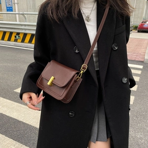 Sac à bandoulière vintage marron avec boucle dorée porté sur un manteau noir élégant
