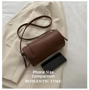 Detail of dark brown cylindrical shoulder bag shown with phone for size reference