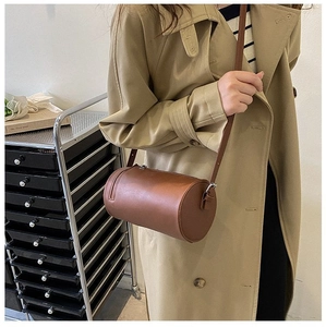 Brown leather cylindrical crossbody bag shown with a tan trench coat for a stylish urban look