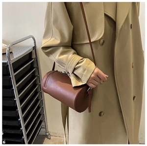 Brown leather cylinder bag shown on a model wearing a khaki coat for stylish look