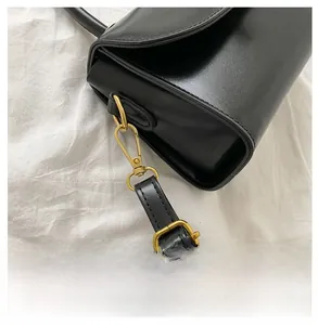 Detail shot of black leather handbag with reinforced gold metal hooks and adjustable strap