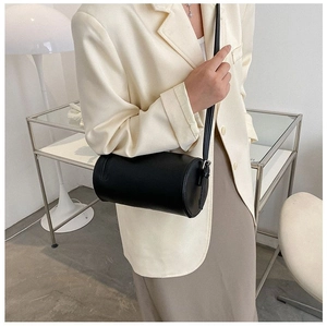 Modern black cylindrical leather shoulder bag shown on model in a minimalist room