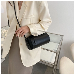 Minimalist black cylinder crossbody bag shown on model with neutral fashion outfit