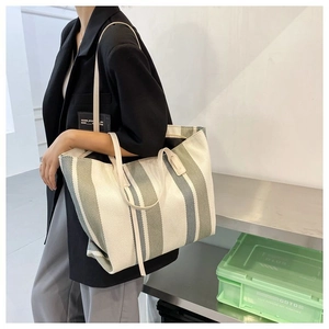 Dettaglio della grande borsa tote in tela a righe con doppi manici indossata da modella