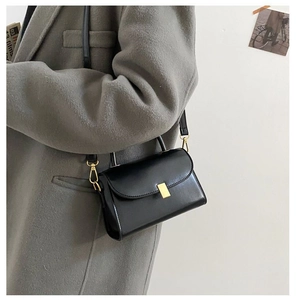 Close-up of a black glossy crossbody bag with golden buckle on a grey woolen coat