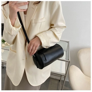 Detail of a black cylindrical crossbody bag with smooth matte finish and slim shoulder strap