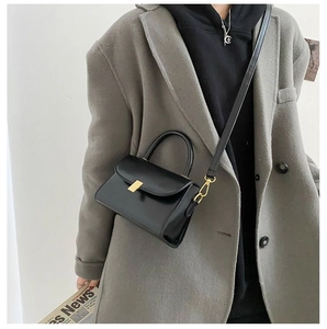Fashionable black leather crossbody bag with golden lock shown on a winter coat