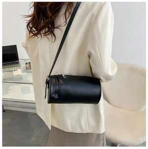 Detail of a black cylindrical crossbody bag with silver zipper shown on a model