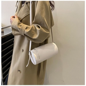 Lifestyle view of a minimalist white cylindrical crossbody bag paired with a classic trench coat