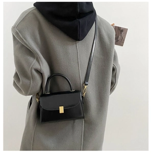 Detail of a minimalist black leather crossbody bag with a sleek gold metal buckle