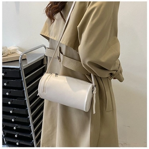 Detailed view of a white leather cylinder crossbody bag styled with a khaki trench coat