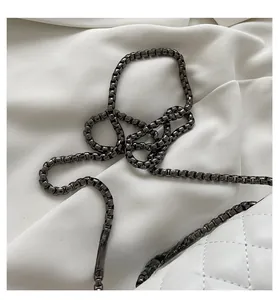 Detail of gunmetal box chain on white quilted leather bag over silk fabric