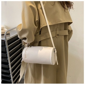 Minimalist beige cylindrical crossbody bag shown worn by a model in a lifestyle setting
