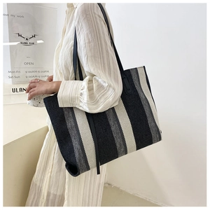 Dettaglio di una grande borsa tote in tela a righe con spalline nere in un interno luminoso