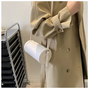 Detail of white cylinder barrel bag on shoulder with adjustable strap and leather texture