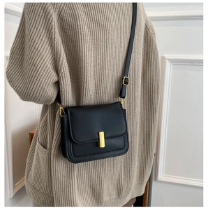 Gros plan sur le sac bandoulière en cuir noir mat avec fermoir rectangulaire doré