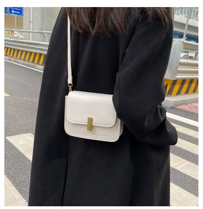 Petit sac bandoulière blanc minimaliste avec fermoir doré sur manteau noir
