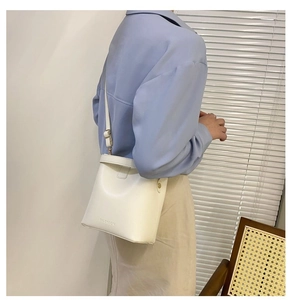 Detailed shot of white leather bucket bag with FASHION logo and adjustable strap
