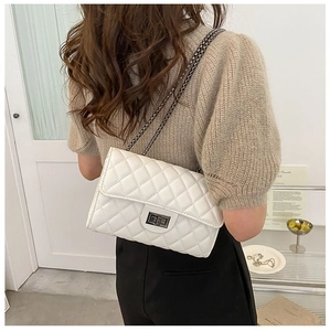 Detail view of a white quilted crossbody bag with silver chain strap on a model