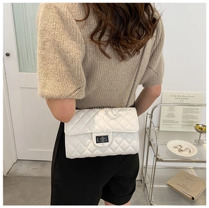 Close-up of white quilted chain bag with silver lock on model in a soft indoor setting