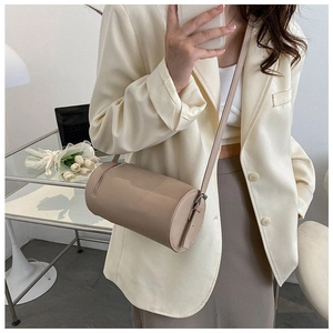 Detail of a minimalist beige cylindrical crossbody bag with a slim matching shoulder strap