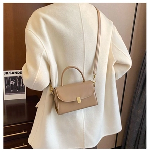Beige leather crossbody bag with gold lock and top handle shown on a model