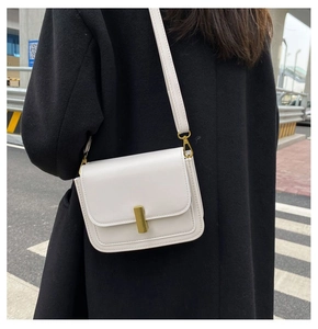 Sac à bandoulière en cuir blanc avec boucle dorée porté sur un manteau d'hiver noir