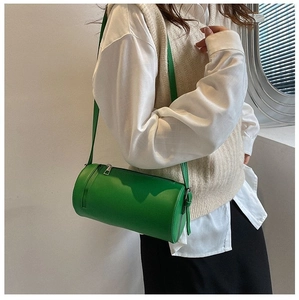 Green cylindrical crossbody bag worn by a model in a minimalist stylish setting