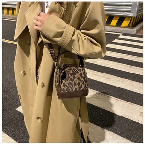 Detail of leopard print bucket bag with brown leather handles worn with khaki trench coat