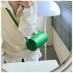 Close-up of green cylinder crossbody bag with smooth leather texture and adjustable strap