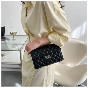 Quilted black chain crossbody bag worn by a model in a minimalist indoor setting