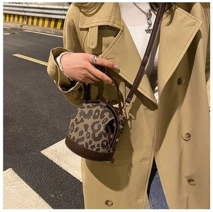 Detailed view of leopard print bucket bag with brown leather straps in city street setting