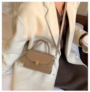 Detail of a khaki leather crossbody bag with a gold clasp in a stylish urban setting