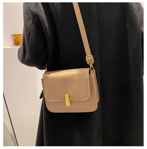 Détail d'un sac carré en cuir beige avec fermoir doré porté sur un manteau noir