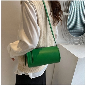 Close-up of a green cylindrical crossbody bag on a model in beige knitwear