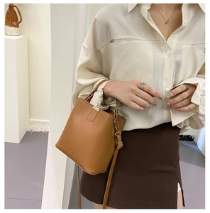 Detail of a brown leather bucket bag with gold hardware worn with a beige shirt