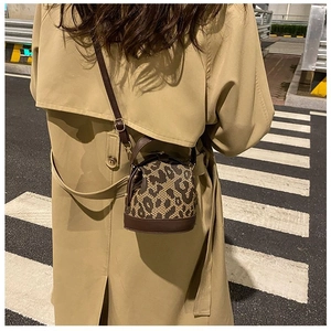 Detail of leopard print bucket bag with brown leather strap worn over a khaki trench coat
