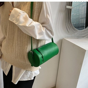 Detail of a bright green cylinder crossbody bag in high-quality leather and metal buckles