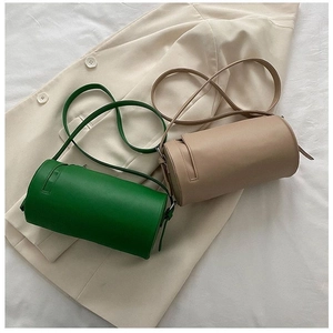 Top view of green and beige cylindrical crossbody bags on a beige blazer background