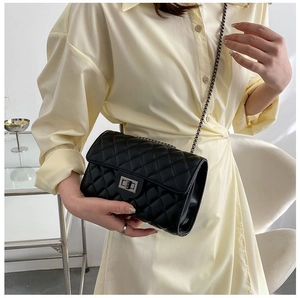 Detail of black quilted chain bag with silver twist lock on a minimalist model