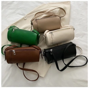 Five colored cylindrical shoulder bags displayed on beige blazer and white fabric