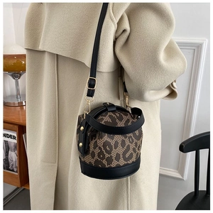 Chic leopard print cylinder bucket bag styled with a beige coat in a warm indoor setting