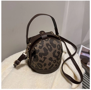 Detail of round leopard print bag featuring brown leather handles and gold-tone hardware