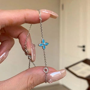 Close-up of a silver clover bracelet with blue enamel and crystal charm on a hand