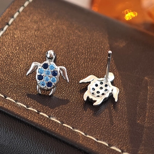 Blue crystal sea turtle stud earrings in silver finish on premium leather background