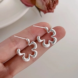 Elegant geometric hollow flower stud earrings in silver finish held by hand