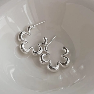Macro view of silver geometric flower stud earrings placed inside a white ceramic bowl