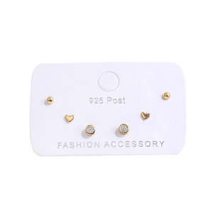 Close-up of three pairs of gold heart, bead, and crystal studs on a white display card