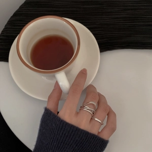 Set di anelli d'argento incrociati indossati dalla mano che tiene una tazza di caffè