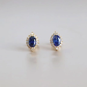 Vue détaillée des boucles d'oreilles saphir bleu ovale avec un halo de zircons brillants